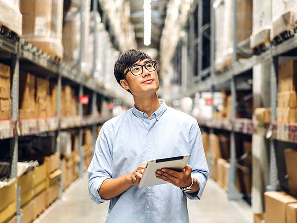 photo of an asian man holding a clip board looking up at stock in a warehouse