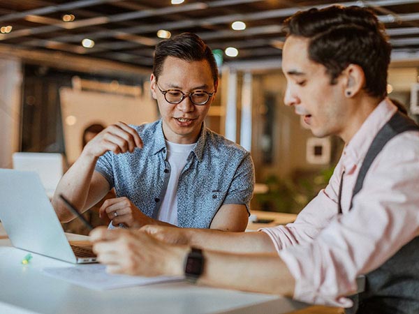 2 people in sitting at a table in front of a laptop