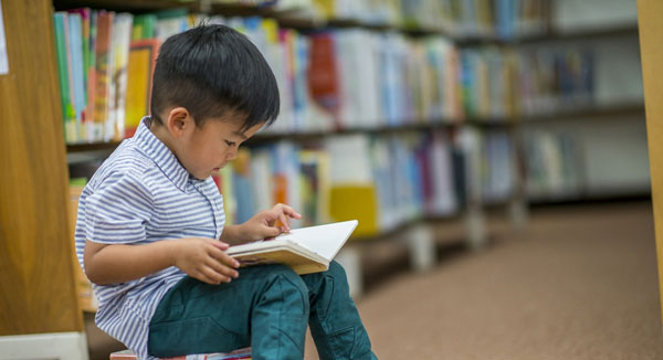un petit garçon en train de lire, assis sur des livres