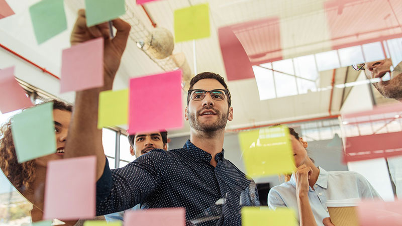 Man leading a conversation with co-workers and organizing ideas on post-it notes
