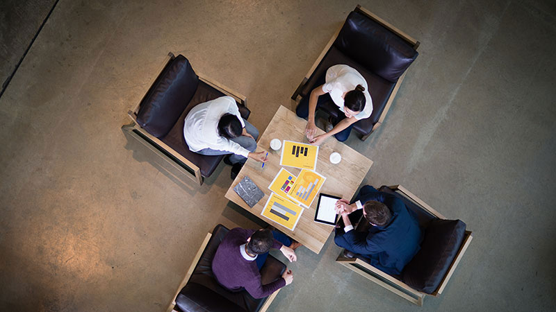 Top view of four team members collaborating around a square coffee table
