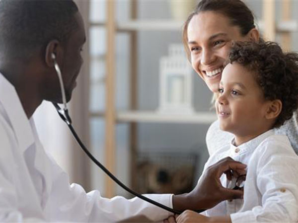 Medical staff member holding a stethoscope to a child's chest with a parent in the background