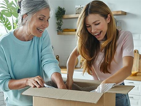 Happy senior woman and her adult daughter unpacking box while standing at the domestic kitchen