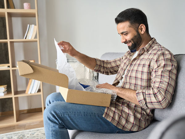 Happy man opening box with ordered goods at home on couch.