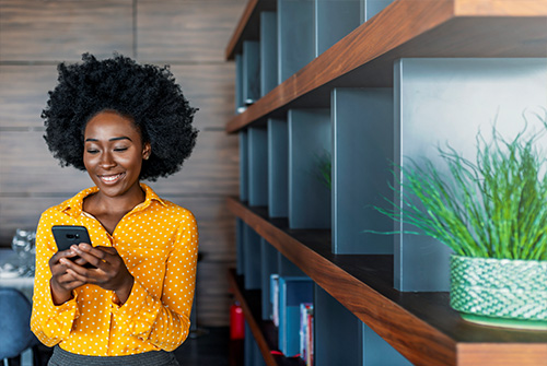 woman on her phone standing next to a book shelf