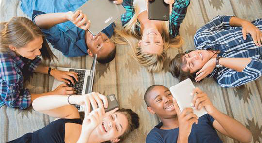 a group of millenials laying in a circle engaged with different technological devices