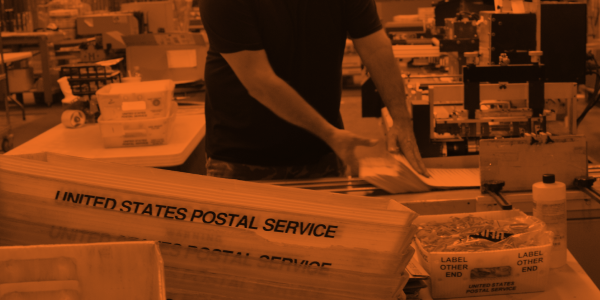 Man putting paper bundle into Postal Services mailing box.