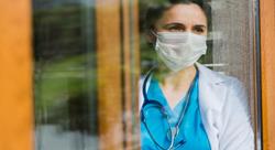 female doctor wearing a face mask looking out a hospital window