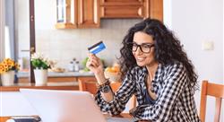 woman sitting in her kitchen in front of a laptop smiling while she holds up one of her credit cards