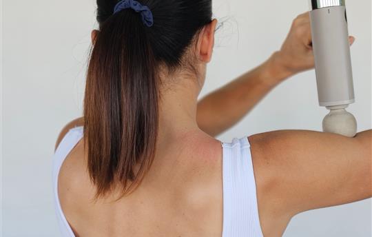 Person using a massage device to relieve tension on the shoulder and back at home concept