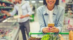 Woman pushing a shopping car in the supermarket, looking at her phone