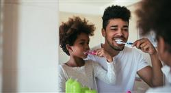 Father and daughter brushing their teeth in front of bathroom mirror