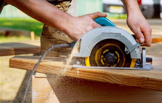 Builder saws a board with a circular saw cutting a wooden plank