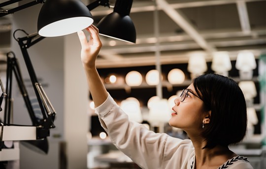 Asian young short hair woman wearing glasses choosing new lamp to buy at furnishings light
