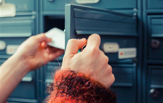person in sweater opening blue mailbox