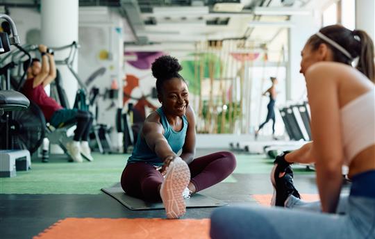 Happy woman warming up with her female friend during sports training in gym