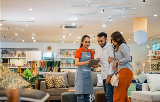 female shop assistant serving male and female customers with a tablet at a furniture store 