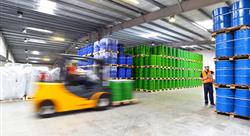 forklift and two workers in orange vests in a warehouse filled with blue and green drums stacked to the ceiling
