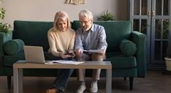 Smiling elderly spouses paying bills online using laptop