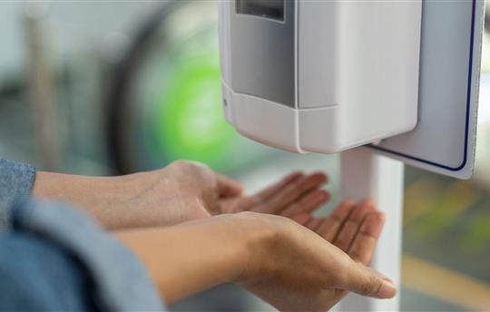 Close up of woman holding hands under automatic sanitizer dispense