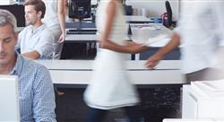 man looking at a large monitor with office workers at work behind him