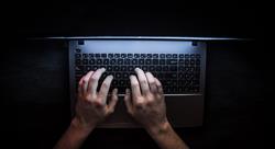 The hands of a hacker type on a keyboard in the dark