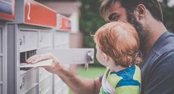 father holding infant son while collecting mail from a community mailbox