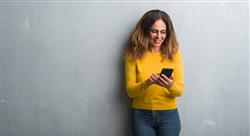 Middle aged woman in yellow sweater using smartphone standing and smiling
