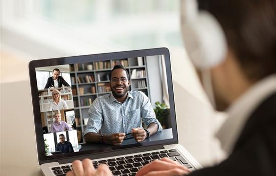 Back view of male employee talking on video call with diverse smiling colleagues