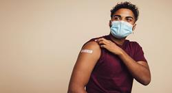 man wearing mask pulling up shirt sleeve to show his vaccination bandaid