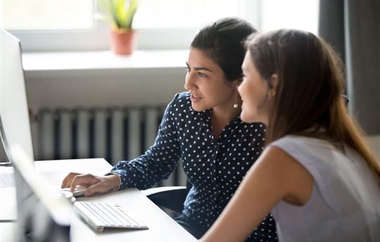 Smiling female colleagues work together at computer