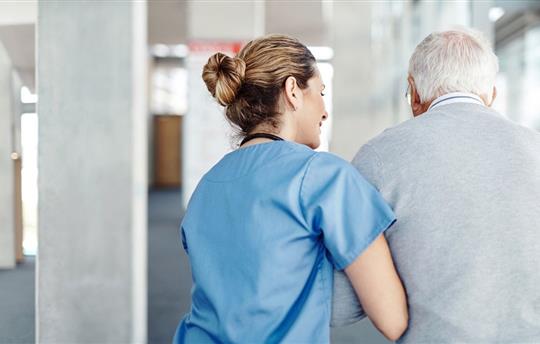 healthcare worker escorting elderly man down hospital hallway