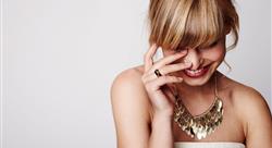 female smiling and wearing a gold ring and gold necklace