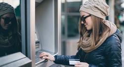 female millennial in winter coat and hat at an atm holding a debit card