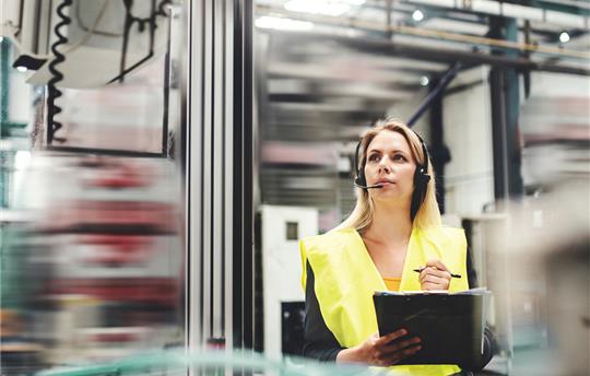 Woman wearing a yellow safety vest and ear protection in an industrial setting