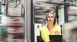 Woman wearing a yellow safety vest and ear protection in an industrial setting