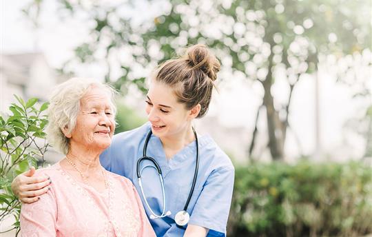 Young nurse in scrubs with her arm around an elderly patient