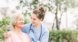 Young nurse in scrubs with her arm around an elderly patient