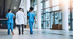 two healthcare workers in blue scrubs and one in a white coat walking and talking together through hospital lobby