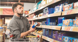 Man stands in a supermarket with a bundle of biscuits in his hands and looks at the shelf with sweets.