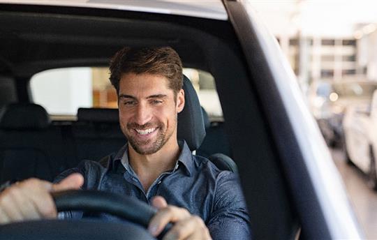 man sitting behind steering wheel of car inside dealer showroom
