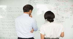 two researchers looking at a whiteboard with notes and equations scribbled on it