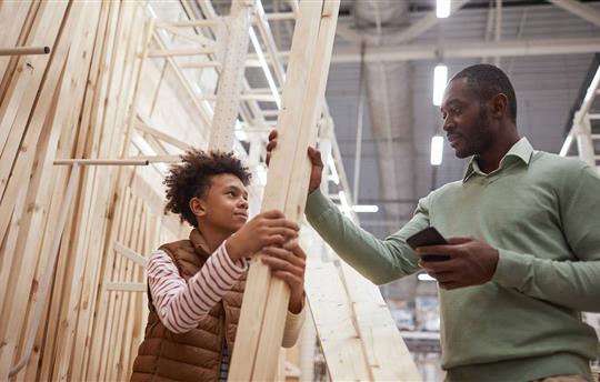 Low angle portrait of father and son shopping together in hardware store and choosing wooden boards for home improvement project