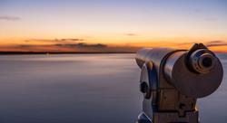 A telescope on a lookout at a beautiful sunset and a long exposure of the water on the sea.