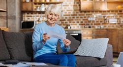 Woman with white hair seated on a couch reading mail
