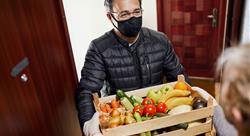 Man in black reusable face mask delivering crate of vegetables to elderly woman