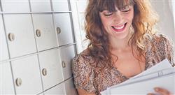 smiling woman leaning on a bank of mailboxes while reading her mail