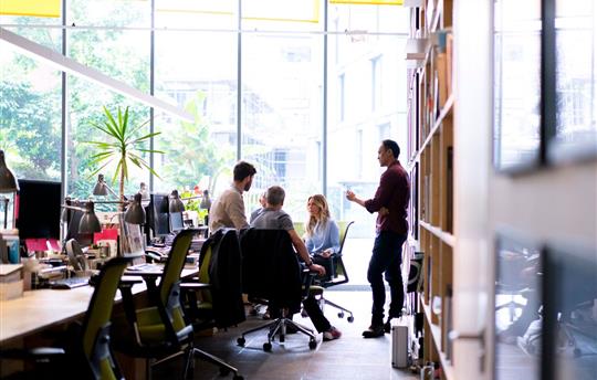 five business professionals in an open office setting having a discussion