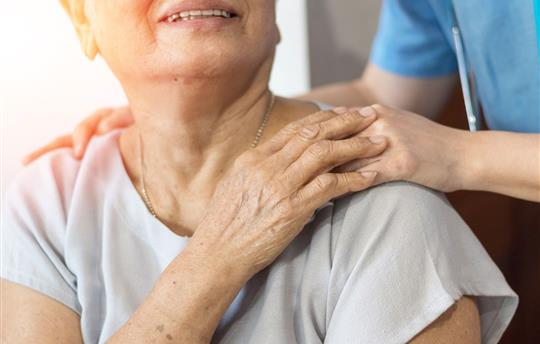 healthcare worker in blue scrubs placing hand gently on senior woman's shoulder