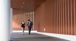 two people in business attire walking down an outdoor corridor having casual conversation